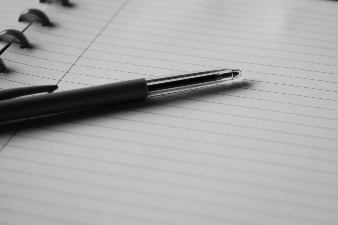Black and white image of a pen resting on an open lined notebook, ideal for writing or note-taking themes.